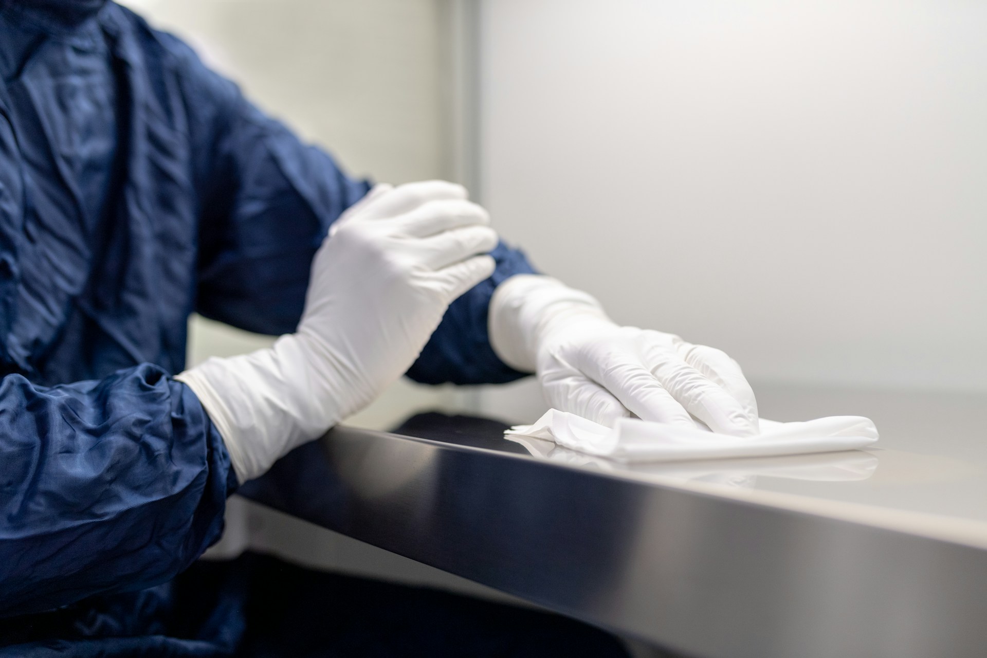 Gowned researcher wiping down a stainless steel surface in a controlled cleanroom environment