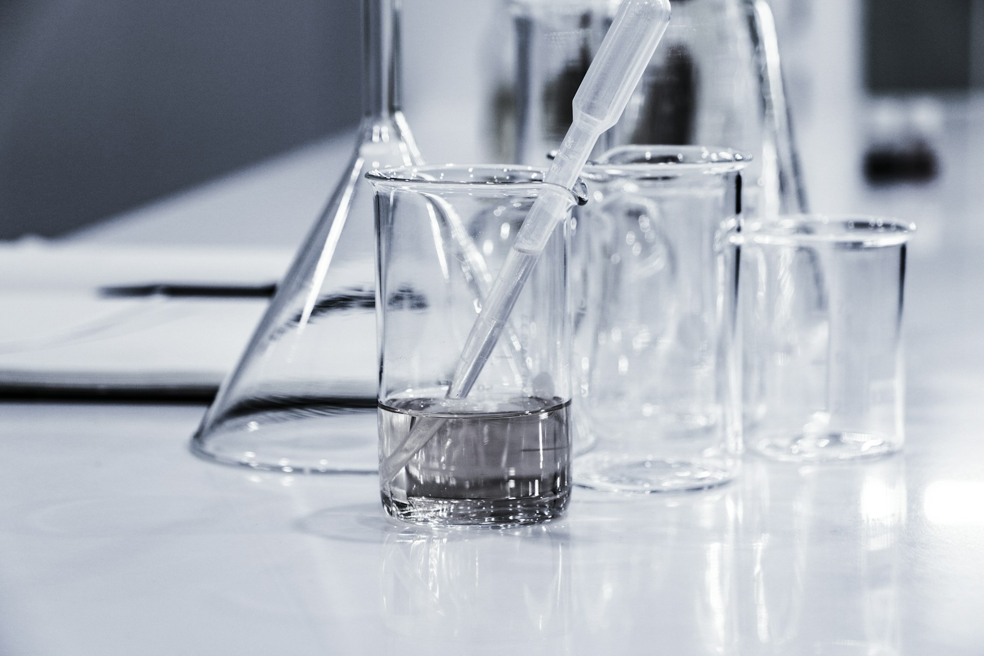 Laboratory beakers and a flask holding clear water-based solutions with a pipette